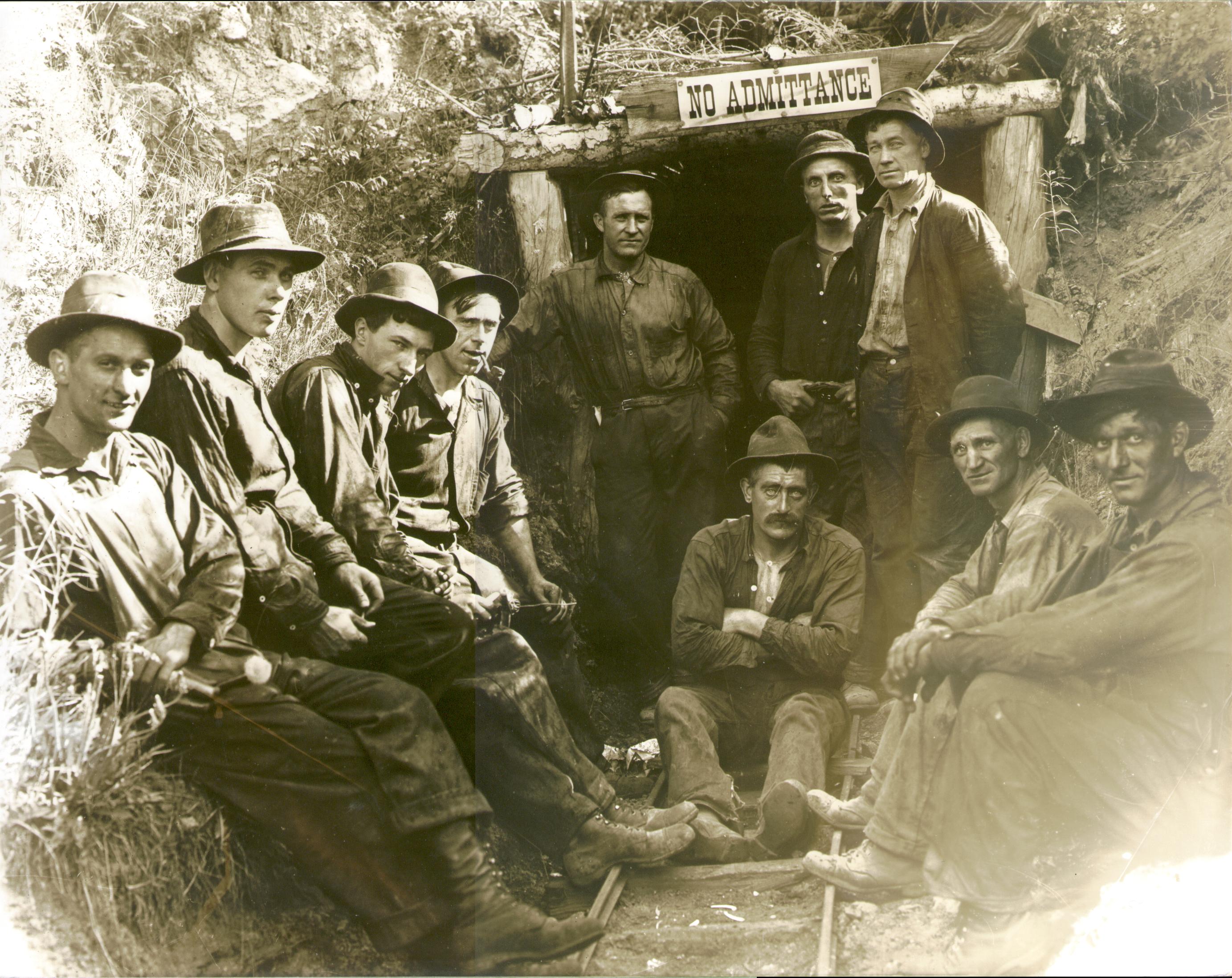 Ten miners wearing felt hats and work clothes outside a mine entrance