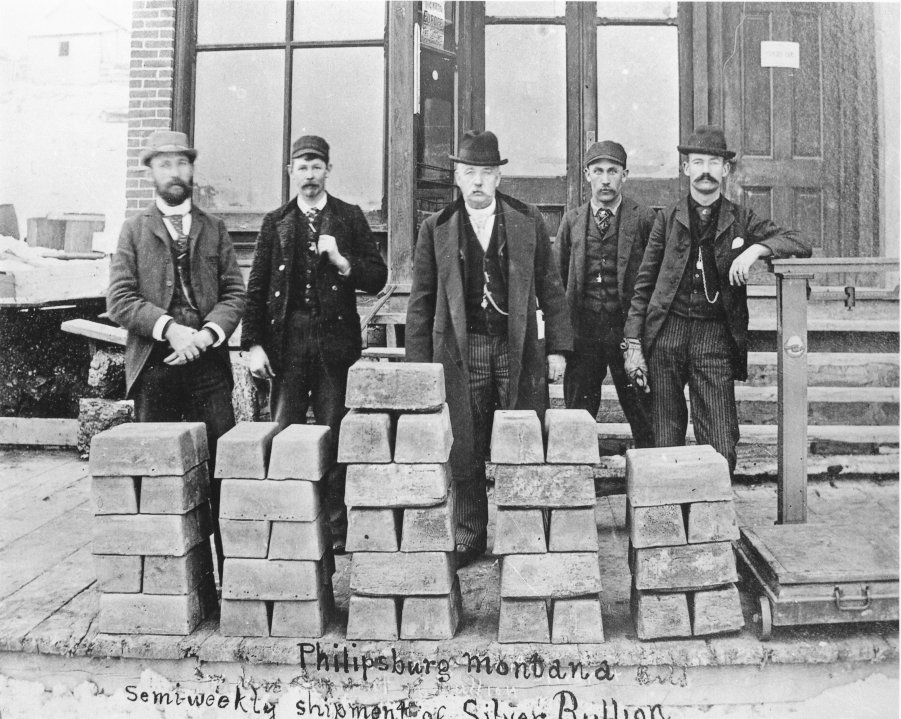 Five men standing behind stacks of silver bullion bars