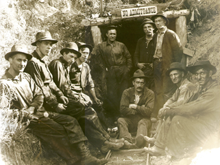 Ten miners wearing felt hats and work clothes outside a mine entrance